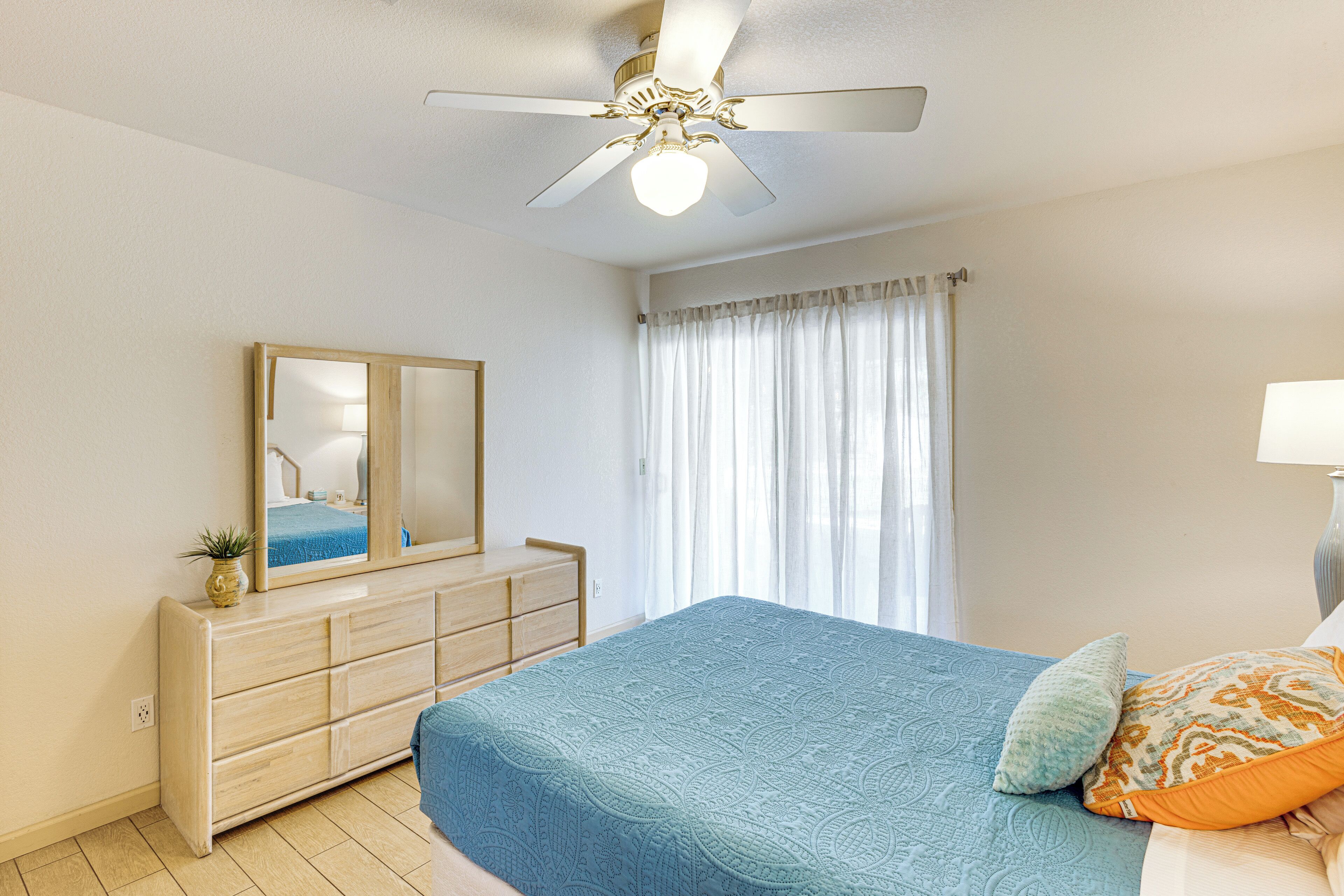 A bedroom with a bed, a dresser, a ceiling fan, a window with curtains, and a mirror.