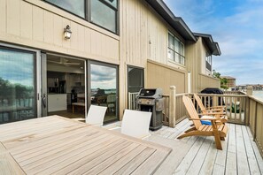 Una terrazza con tavolo e sedie in legno, un barbecue e una porta scorrevole in vetro che dà su una cucina.