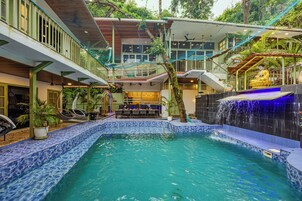 Uma área de piscina com uma cascata, assentos e uma escadaria que dá acesso a um andar superior.