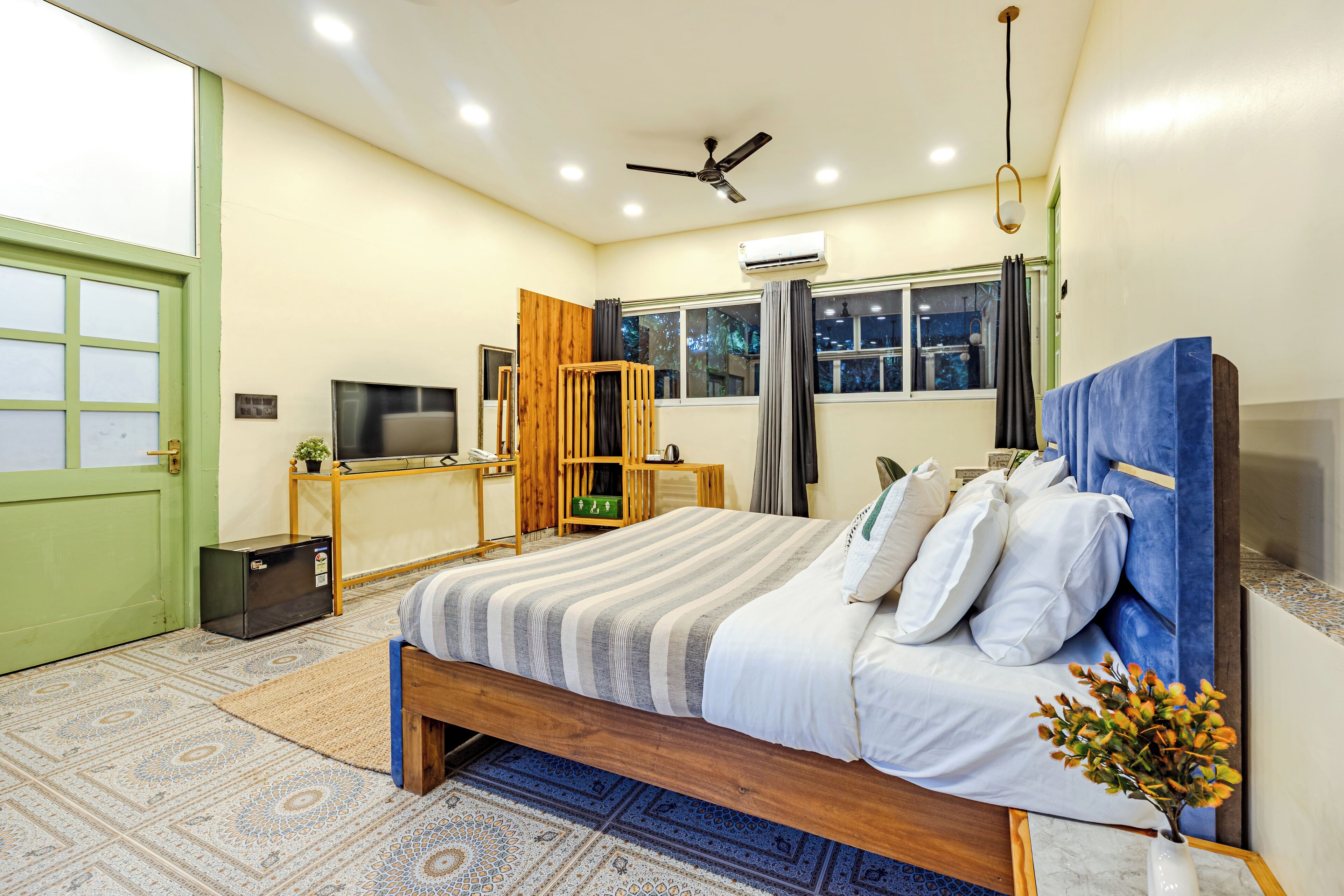 A neatly arranged bedroom with a bed, a desk, a television, and a window with curtains.