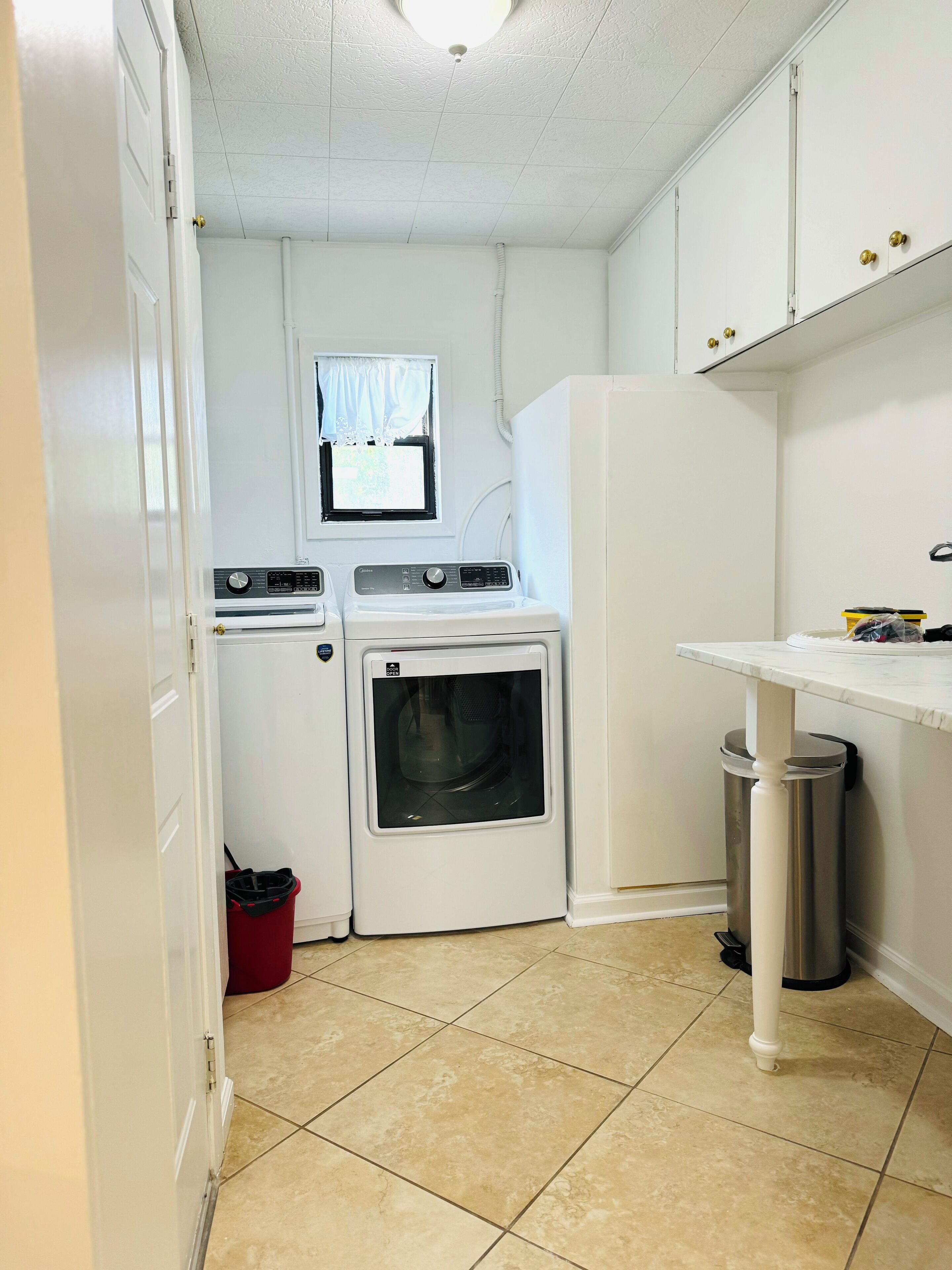 A compact laundry room with a washing machine, dryer, and a small trash bin.