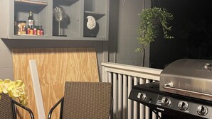 Una zona de cocina con una parrilla, sillas de mimbre, una mesa de madera y una planta en maceta.