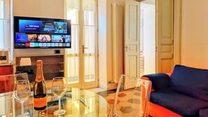 Een woonkamer met een flatscreen televisie, een glazen tafel met een fles champagne en een blauwe bank.