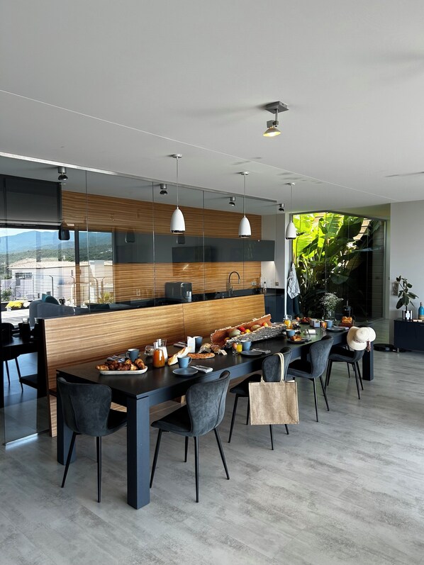 Una cocina moderna con una larga mesa de comedor, múltiples sillas e iluminación colgante.