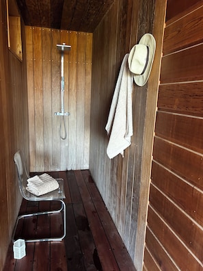 Una cabaña de madera con ducha, una silla transparente y un sombrero en la pared.