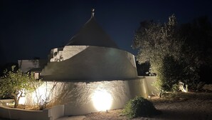 A building with a conical roof and a circular base, surrounded by trees and a landscaped area with a pathway. - Trullisetto: the authentic heart of Apulia (Puglia)