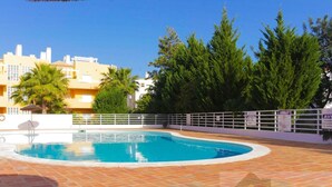 A swimming pool with a tiled deck, surrounded by a white fence and greenery.