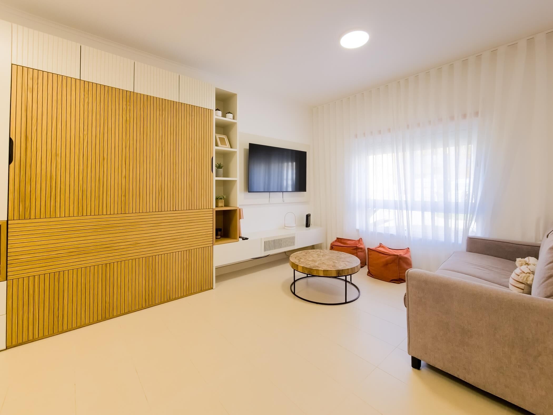 A modern living room with a large wooden cabinet, a flat-screen TV, a beige sofa, and a round coffee table.