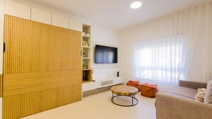 A modern living room with a large wooden cabinet, a flat-screen TV, a beige sofa, and a round coffee table.