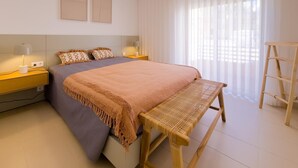 A bedroom with a bed, bedside tables, a bench, and a window with sheer curtains.