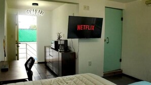 Une chambre avec un lit, un bureau, une machine à café, un téléviseur affichant le logo « NETFLIX » et une porte.