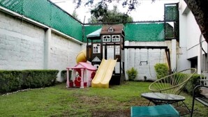 Une cour arrière clôturée avec une cabane de jeux, un toboggan et une chaise.