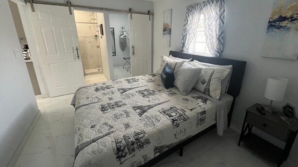 A bedroom with a bed featuring a cityscape design, a ceiling fan, a nightstand with a lamp, and a window with patterned curtains. - Charming guesthouse B 1-bedroom in North Lakeland with full kitchen, WiFi, AC (Lakeland)