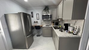 A compact kitchen with a stainless steel refrigerator, a microwave, and a sink. There are bar stools and a countertop with various items. - Charming guesthouse B 1-bedroom in North Lakeland with full kitchen, WiFi, AC (Lakeland)