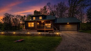 A log cabin with a porch, a garage, and a well-maintained lawn. - The Alibi Cabin - Pool, Hot Tub & Private Trails - Secluded 17-Acre Retreat (Kensington)