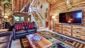 A log cabin interior with a leather sofa, a TV, and a stone wall. - The Alibi Cabin - Pool, Hot Tub & Private Trails - Secluded 17-Acre Retreat (Kensington)