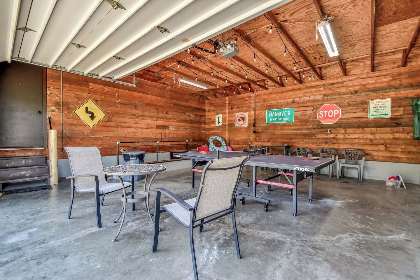 A spacious indoor area with tables and chairs, wooden walls, and various signs including 'HANOVER TOWNSHIP LIMIT' and 'NO PARKING.'