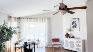 Een moderne woonkamer met een ronde tafel, stoelen, een plafondventilator, een witte kast en een lijstwerk kunstwerk aan de muur.