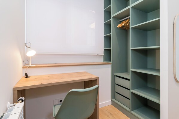 Een werkruimte met een houten bureau, een stoel, een whiteboard en een rek met kleding.
