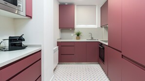 Une cuisine compacte avec des placards roses, un four à micro-ondes, une machine à café et une petite fenêtre.
