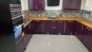 A modern kitchen with purple cabinets, a black refrigerator, and a wooden countertop.