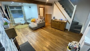 A spacious living area with a grey sofa, wooden flooring, a staircase, and a view of the outdoors.
