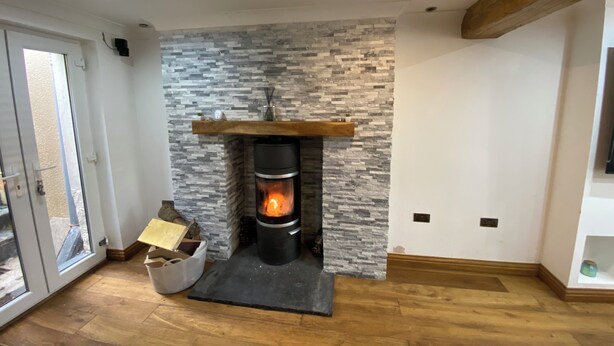 A modern living room with a stone fireplace, wooden beams, and a large window.