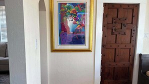 Un corridoio con pavimento in legno, un quadro astratto incorniciato a parete e una porta in legno con maniglia metallica.
