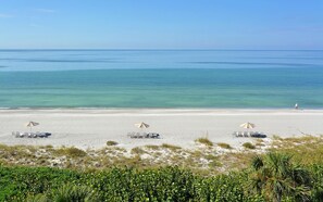 A beach with white sand, clear blue water, and three umbrellas providing shade. - Beachplace 11-501 by FGC (Longboat Key)