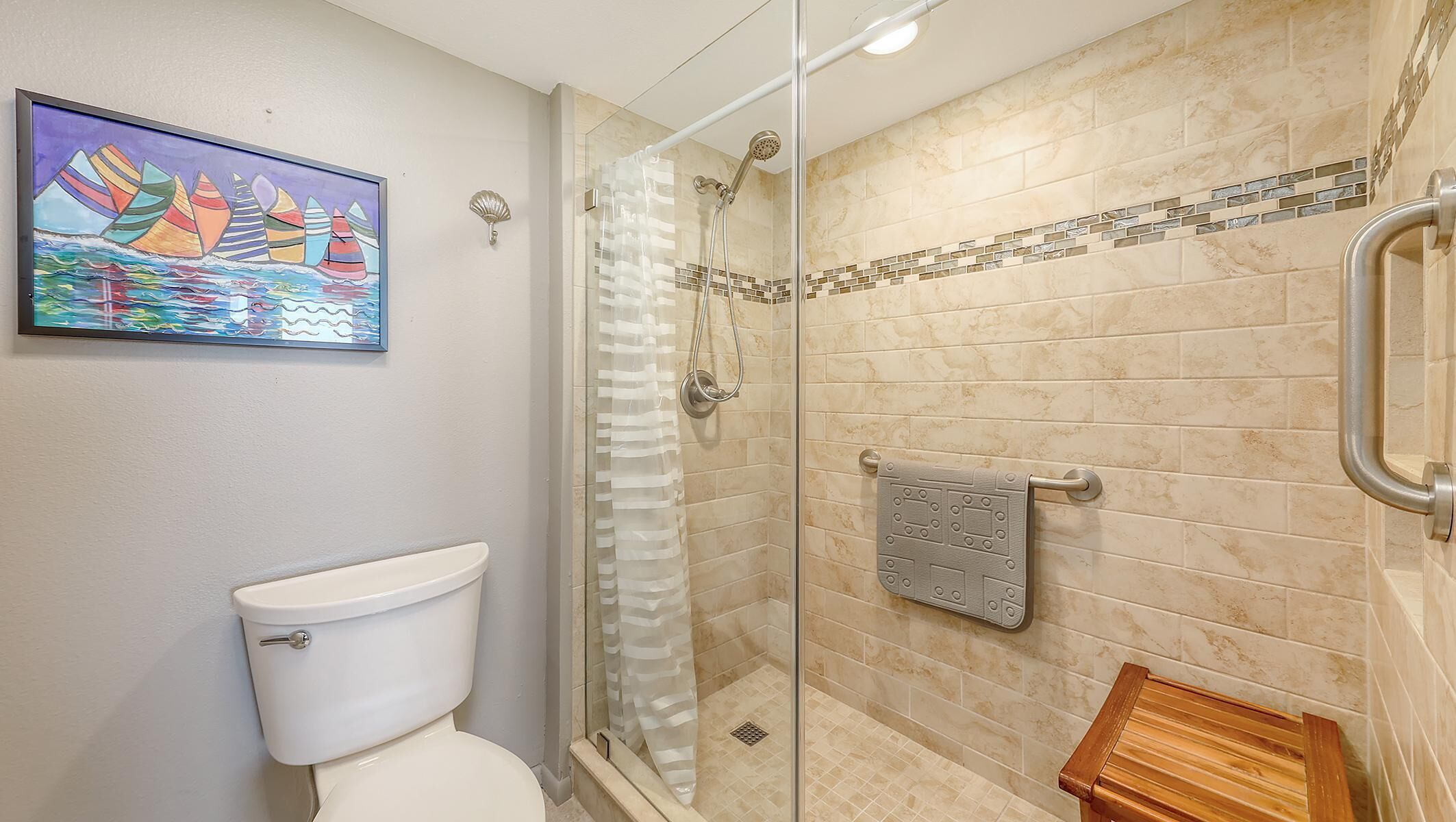 A bathroom with a glass shower enclosure, a toilet, a towel rack, and a small wooden bench.