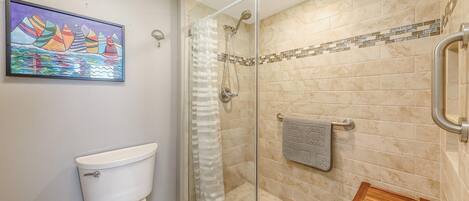 A bathroom with a glass shower enclosure, a toilet, a towel rack, and a small wooden bench.