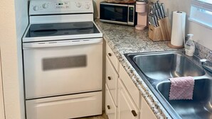 A kitchen with white cabinets, a stove, a microwave, and a sink.