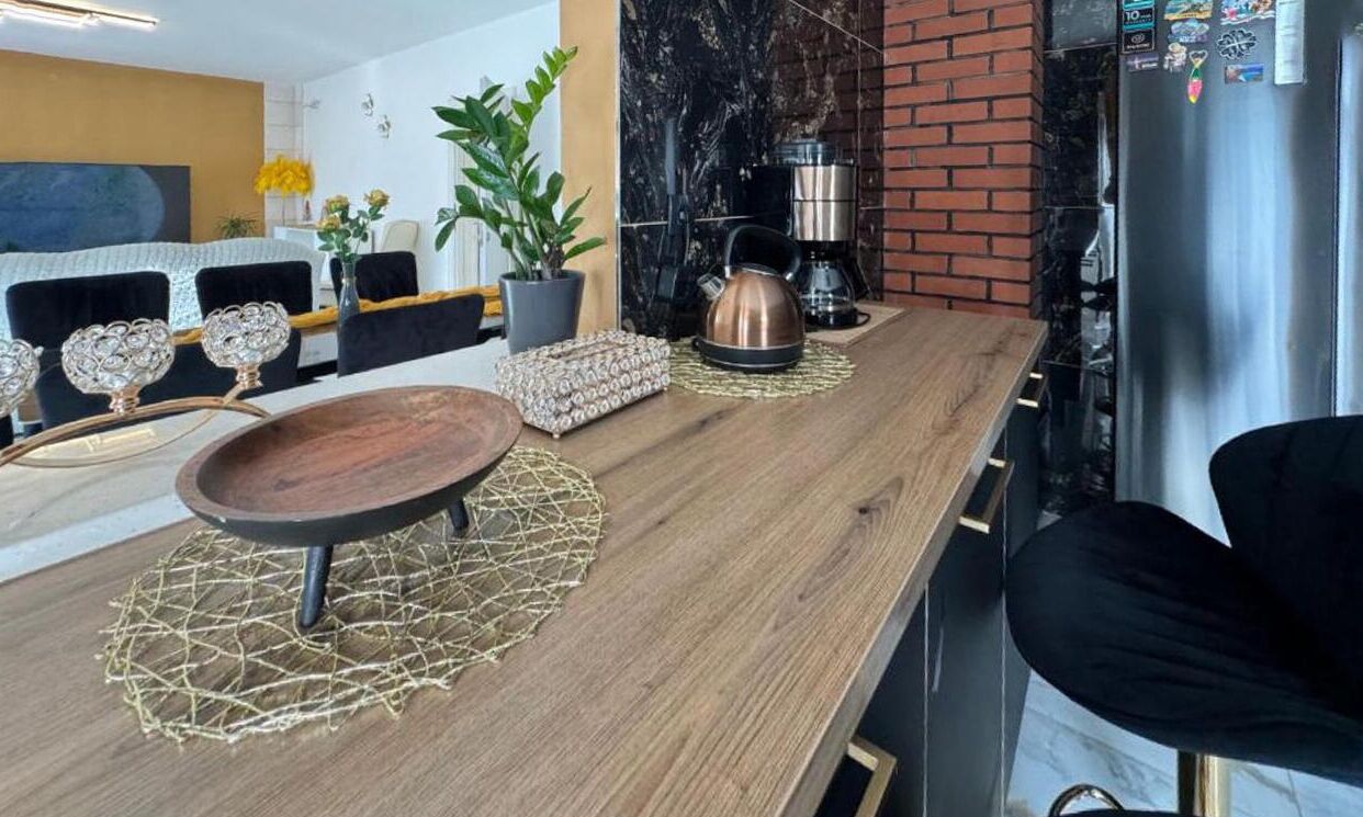 A modern kitchen with a wooden countertop, a kettle, a coffee machine, and a refrigerator.