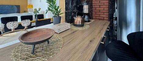 A modern kitchen with a wooden countertop, a kettle, a coffee machine, and a refrigerator.