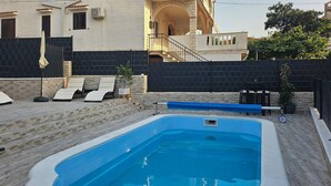 A rectangular swimming pool with a stone deck surrounding it. There are lounge chairs and a small table with chairs nearby. - Beautiful home in Trogir (Trogir)