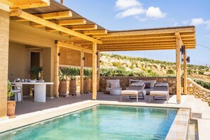 A pool area with a pergola, outdoor seating, and a stone wall backdrop.