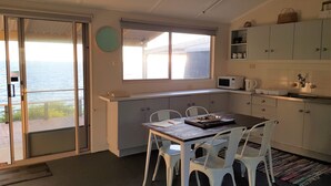 Een compacte keuken met een eethoek, uitzicht op zee en een schuifdeur naar een buitenbalkon.