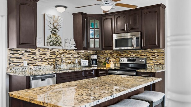 A modern kitchen with dark wood cabinets, a granite island, stainless steel appliances, and a tiled backsplash.