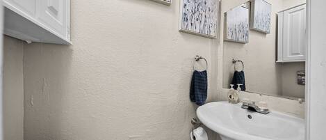 Un baño con lavamanos, inodoro y barra para toallas blancos. Hay dos cuadros con motivos florales en la pared.