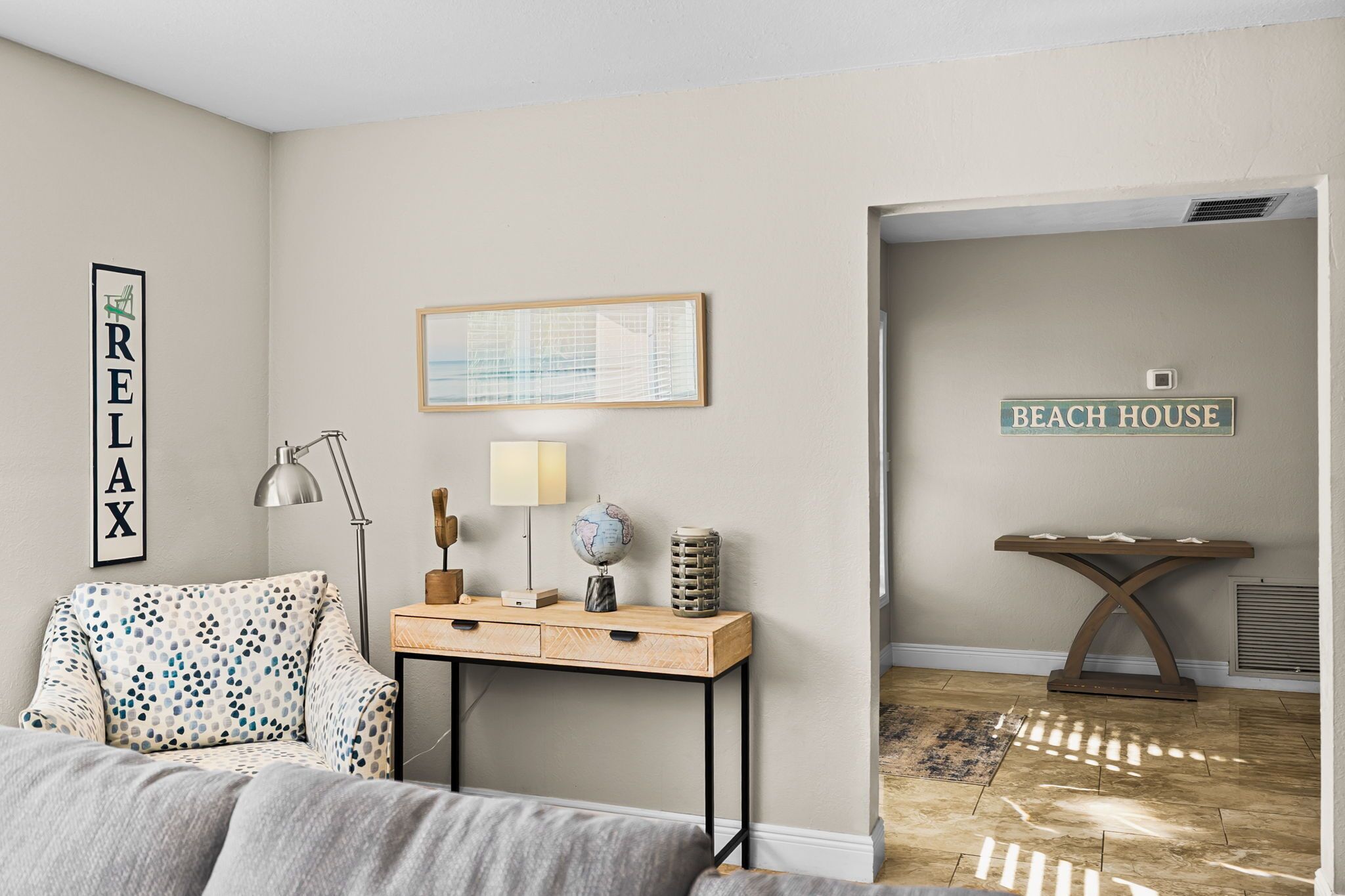 Un dormitorio con cama, escritorio con lámpara, un globo terráqueo y un cuadro enmarcado. En la pared hay un cartel que dice "BEACH HOUSE".