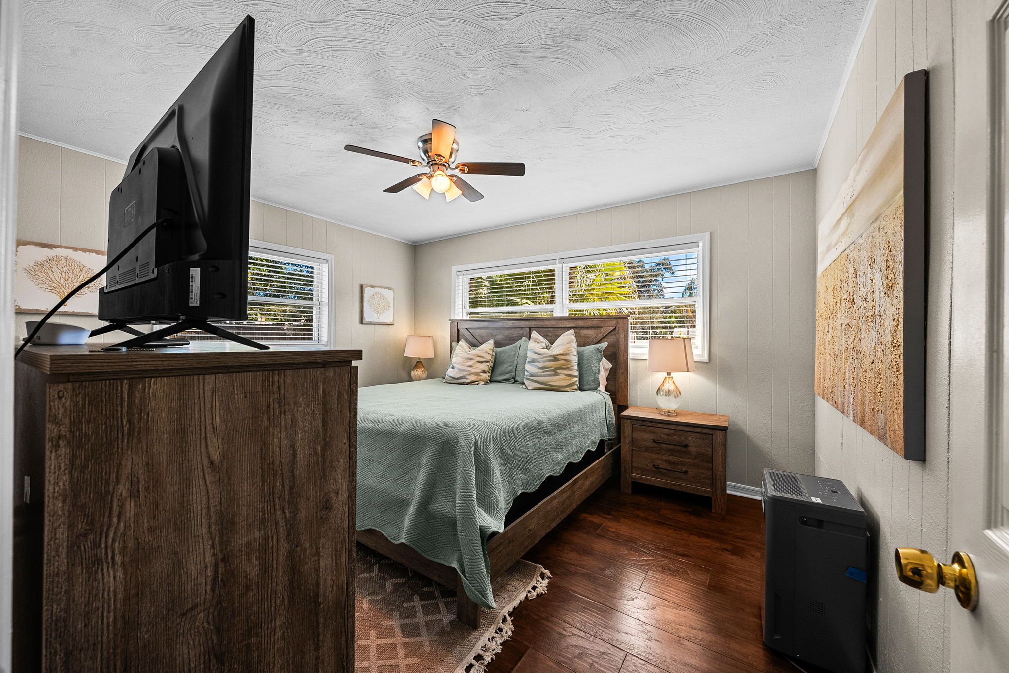 A bedroom with a bed, bedside tables, a ceiling fan, a TV on a stand, and a door with a brass handle.