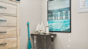A corner room with a wooden cabinet, a small table with a model ship, and a painting of a pier.