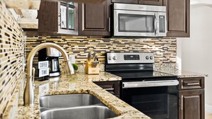 A kitchen with dark wooden cabinets, a stainless steel microwave, a stove, and a coffee maker.