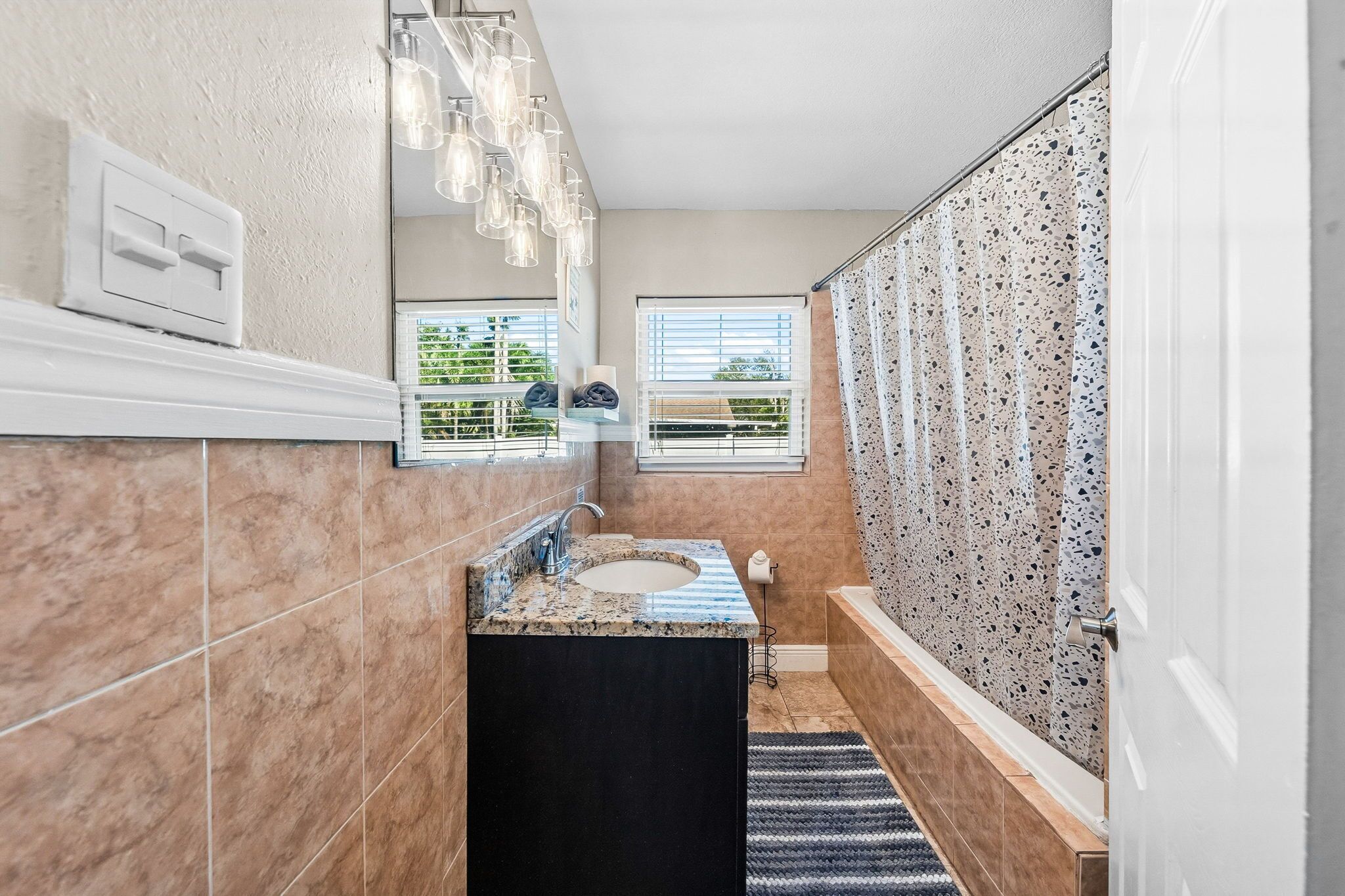 A bathroom with a marble sink, a large mirror, and a shower with a speckled tile wall.