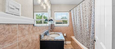 A bathroom with a marble sink, a large mirror, and a shower with a speckled tile wall.