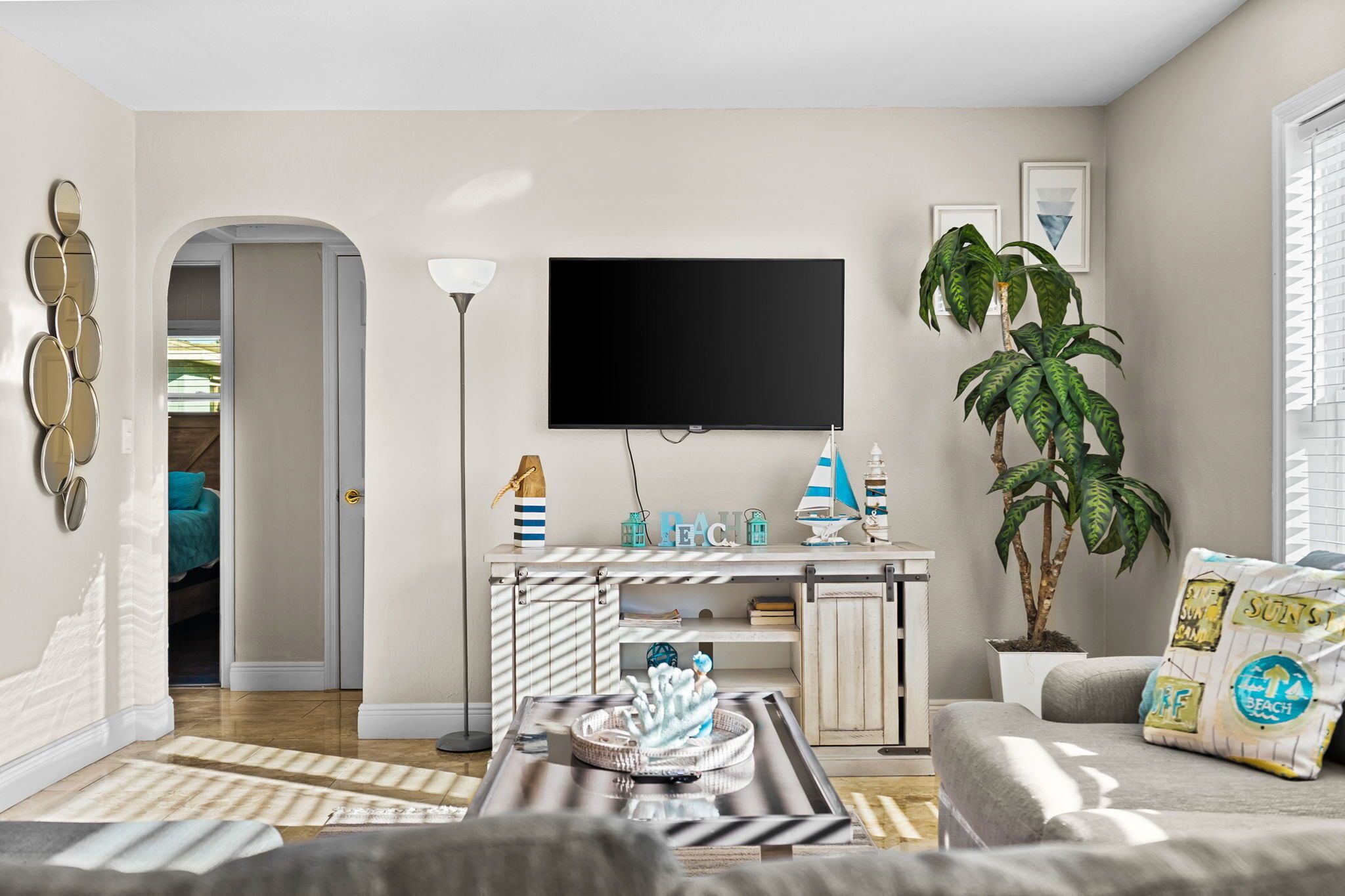 A modern living room with a flat-screen TV, a potted plant, and a sofa with decorative pillows.