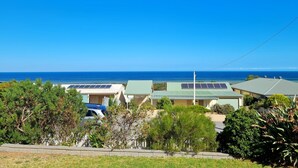 Zona residencial costera con casas que tienen paneles solares, un cielo azul despejado y el océano al fondo.