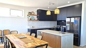 A modern kitchen with dark cabinetry, a central island, and a dining area with a wooden table and chairs. - Jetty Nights, Port Hughes (Port Hughes)