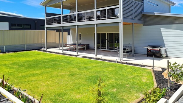Una casa de dos pisos con balcón, un patio con mobiliario exterior y un césped bien cuidado.