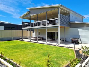 Una casa de dos pisos con balcón, un patio con mobiliario exterior y un césped bien cuidado.